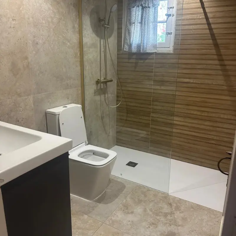 Reforma de baño en Menorca con ducha de obra, pared efecto madera y grifería dorada
